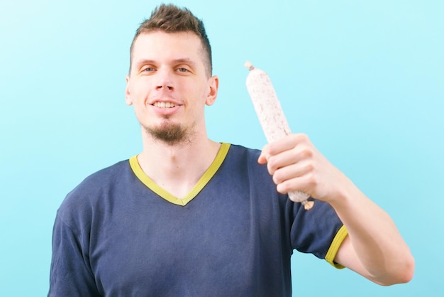 Un uomo sorridente che tiene una salsiccia secca fuet bianco tradizionale su un blu