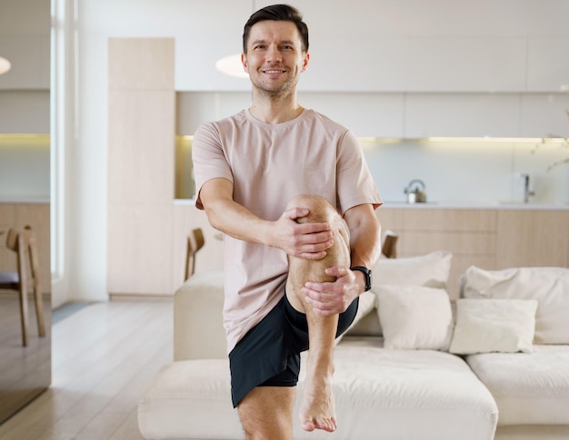 Un uomo sorridente si impegna in una postura di yoga di bilanciamento allungandosi comodamente in uno spazioso sole illuminato