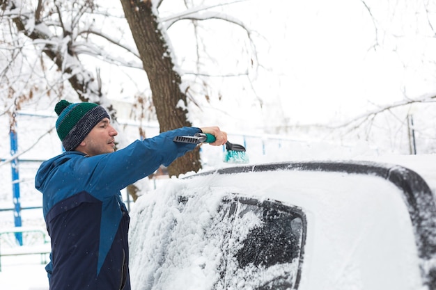 Un uomo spazza la neve da un'auto dopo una nevicata.