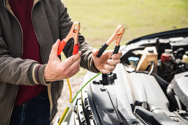 Un uomo sta davanti a un'auto con in mano un ponticello della batteria