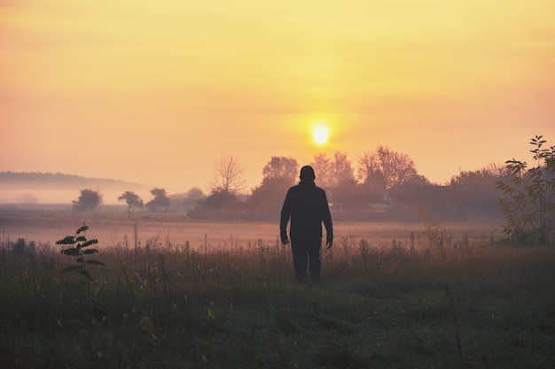 Un uomo sta in riva al lago la mattina presto e guarda l'alba