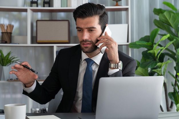 Un uomo sta parlando al telefono e tiene in mano una penna e un laptop.