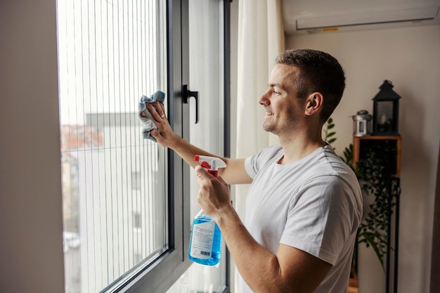 Un uomo sta pulendo la finestra di casa usando detersivo e straccio