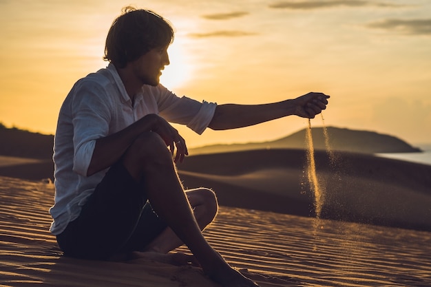 Un uomo sta versando sabbia nel deserto. Sabbia tra le dita del concetto.