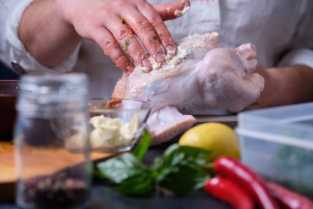 Un uomo strofina il pollo con il burro. Le mani del cuoco nel telaio.