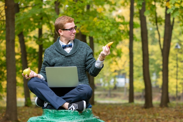 Un uomo su un piedistallo che finge di essere una statua nella posa di un filosofo prima di scegliere una mela o una banana nel parco