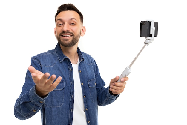 Un uomo su un selfie stick tiene un telefono e trasmette gesticolando verso la fotocamera con un sorriso sul suo