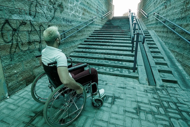Un uomo su una sedia a rotelle siede sullo sfondo delle scale. Il concetto di vita quotidiana grigia dei disabili, problemi di movimento, malattia.