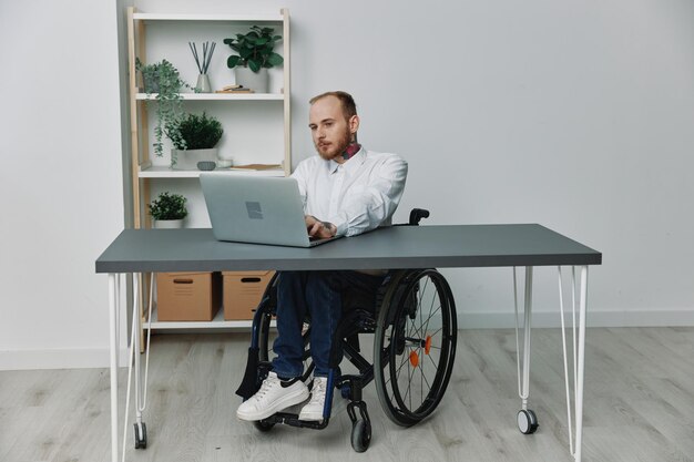 Un uomo su una sedia a rotelle un uomo d'affari con tatuaggi in ufficio lavora a un laptop integrazione nella società il concetto di lavoro una persona con disabilità libertà dai quadri sociali