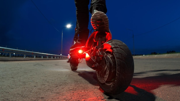 Un uomo su uno scooter elettrico sulla strada Luce stradale notturna da lanterne Vista posteriore del trasporto elettrico moderno e potente