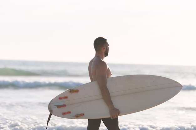 Un uomo surfista con il torso nudo che cammina sulla riva del mare