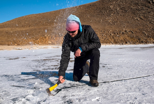 un uomo taglia il ghiaccio con un'ascia su un lago ghiacciato in inverno