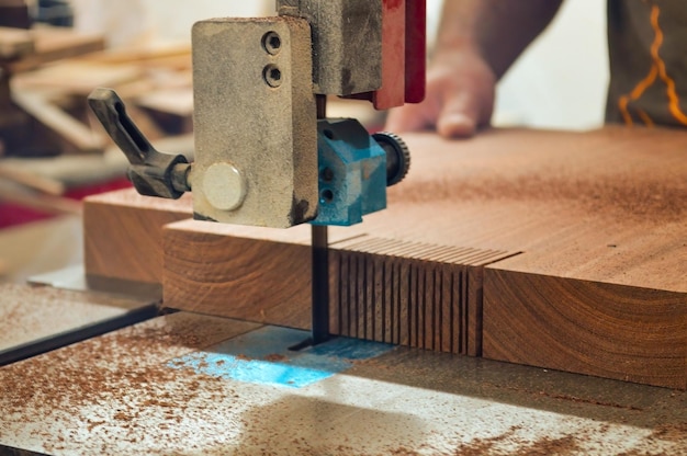 Un uomo taglia il legno con una sega circolare in una sega a nastro da falegnameria che tiene una tavola