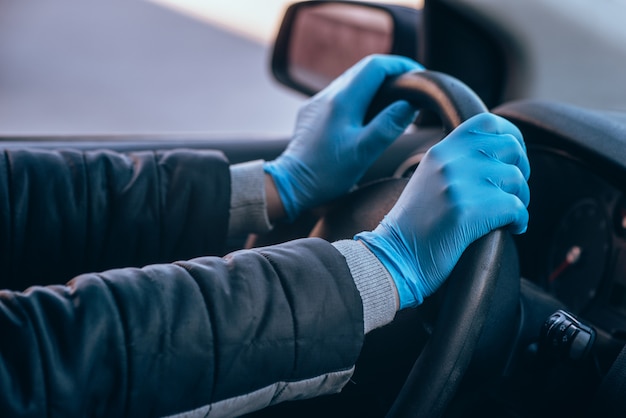 Un uomo tiene il volante di un'auto in guanti medici protettivi. Primo piano delle mani Guida sicura in taxi durante il coronavirus pandemico.