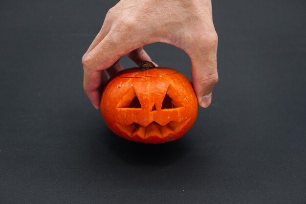 Un uomo tiene in mano una piccola zucca intagliata. Mano con il primo piano della zucca su fondo nero.