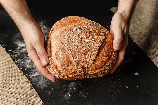 Un uomo tiene tra le mani una pagnotta di pane biologico rustico.