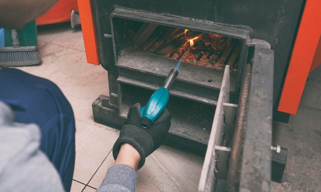 Un uomo tiene un bruciatore a gas e fa un fuoco nella caldaia a combustibile solido nel locale caldaia Combustibile solido e concetto di riscaldamento