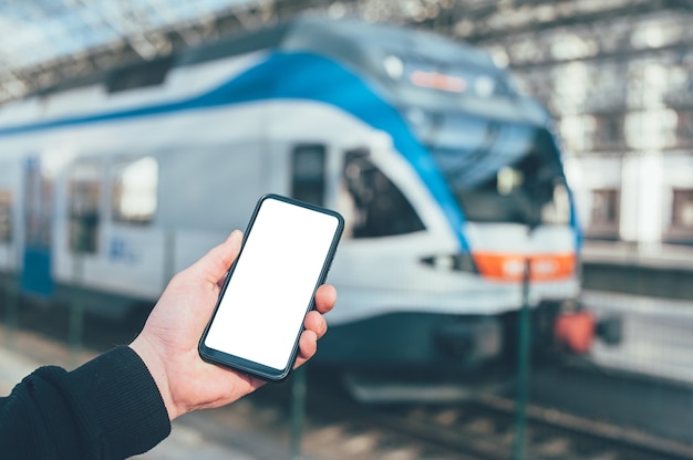 Un uomo tiene un modello di uno smartphone sullo sfondo di un treno in una stazione ferroviaria.