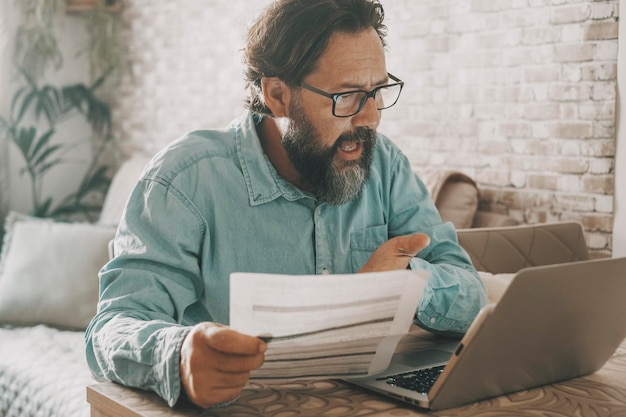 Un uomo urla arrabbiato durante una videochiamata tenendo in mano le bollette Problemi relativi alle persone e ai costi della vita Prezzo dell'energia del gas Un uomo che chiama al computer portatile e spiega problemi con cattiva espressione e stress