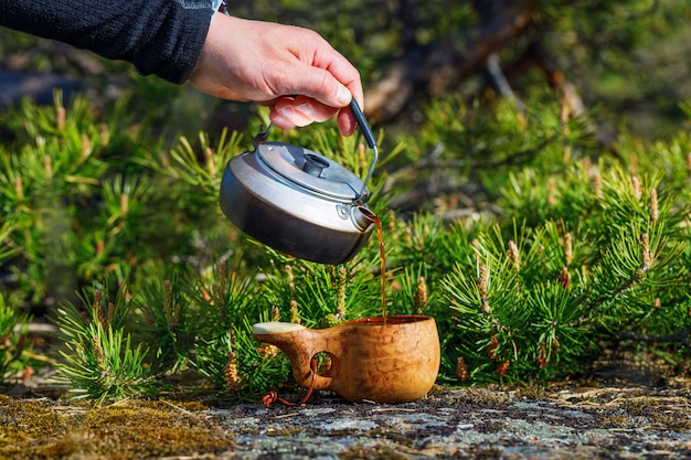 Un uomo versa delizioso caffè da un bollitore in una tazza di legno.