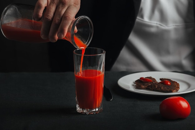 Un uomo versa il succo di pomodoro da un grafico in un bicchiere, accanto ad esso c'è la carne alla griglia fritta su un piatto