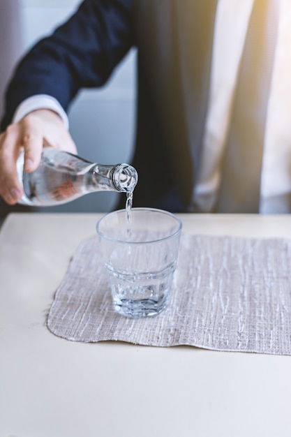 Un uomo versa l&#39;acqua da una bottiglia in un bicchiere vuoto trasparente.