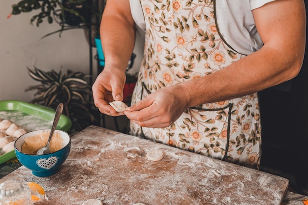 Un uomo vestito con un grembiule e un cappello prepara gli gnocchi in cucina