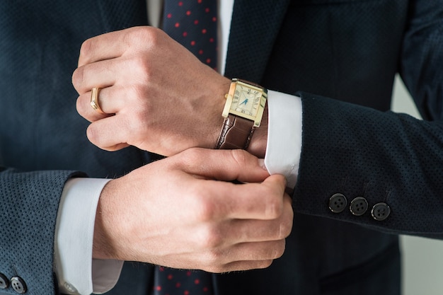 Un uomo vestito con un orologio si abbottona un bottone sulla manica della camicia