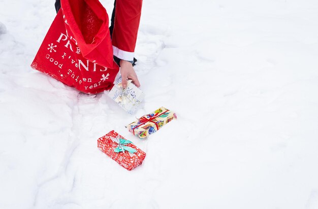 Un uomo vestito da Babbo Natale raccoglie regali in un bosco innevato nella neve, scatole colorate con regali.