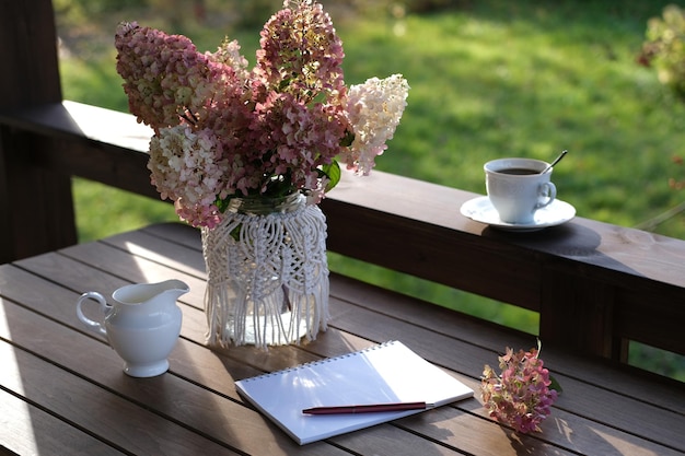 Un vaso con ortensie un taccuino e una tazza di caffè sulla terrazza nel giardino d'autunno