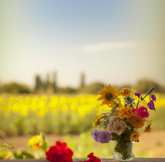 Un vaso di fiori si trova su un tavolo davanti a un campo di fiori.