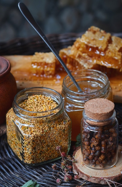Un vaso di vetro con polline, miele e propoli su una tavola di legno si trova su un tavolo di vimini