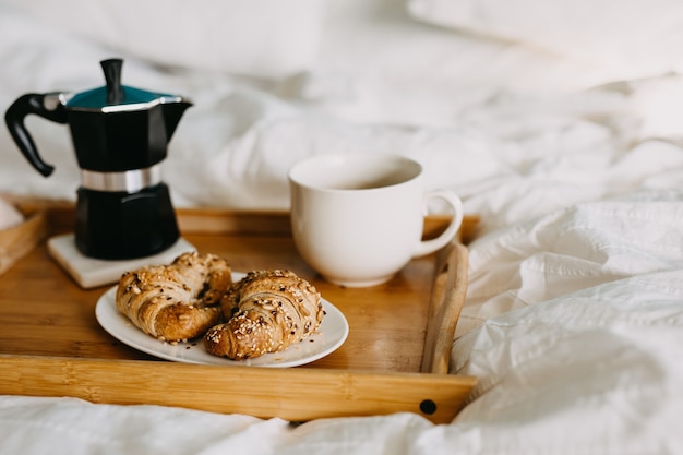 un vassoio di legno con croissant e tazza di caffè sul letto