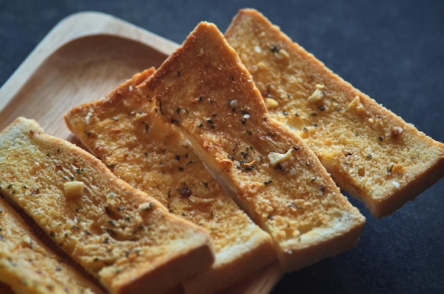 Un vassoio di legno di pane tostato con sopra aglio e pepe.