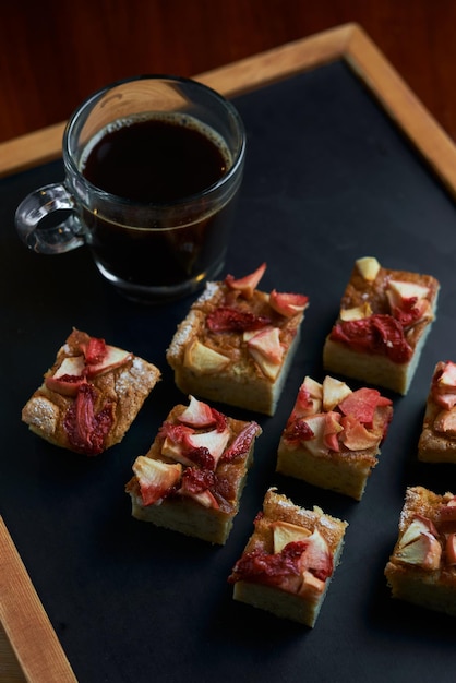 Un vassoio di quadrati di pasta frolla alla mela fruttata con una tazza di caffè sullo sfondo.