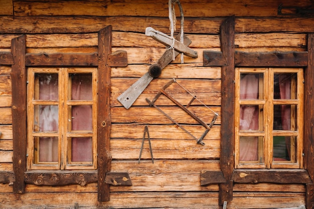 Un vecchio muro di legno di una casa con finestre nel villaggio e strumenti appesi