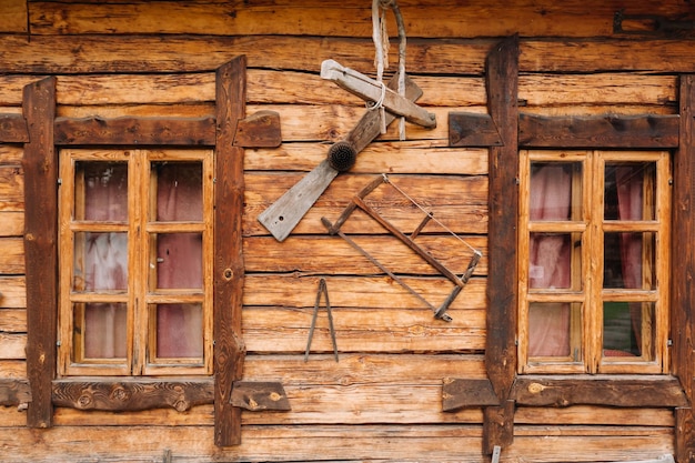 Un vecchio muro di legno di una casa con finestre nel villaggio e strumenti appesi