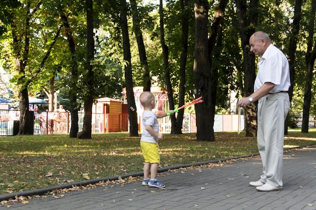 Un vecchio nonno gioca con il nipote nel fine settimana in un parco divertimenti e soffia allegramente bolle di sapone Un anziano un pensionato e un bambino trascorrono del tempo insieme