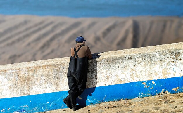 Un vecchio pescatore appoggiato a un muro che guarda verso il mare