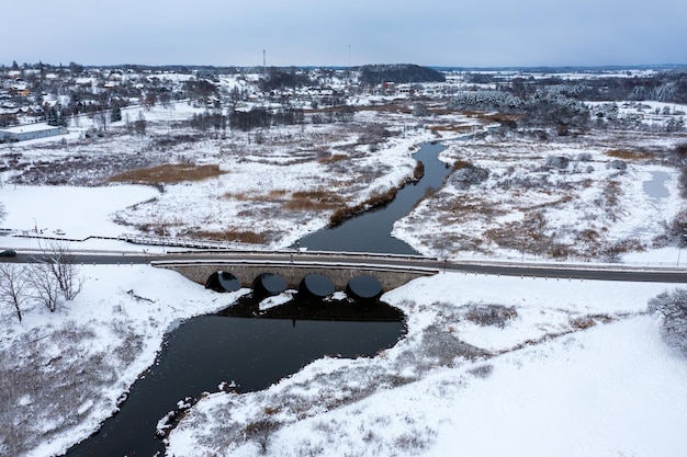 Un vecchio ponte di pietra con archi sul fiume Abava in una giornata invernale nevosa Kandava Lettonia