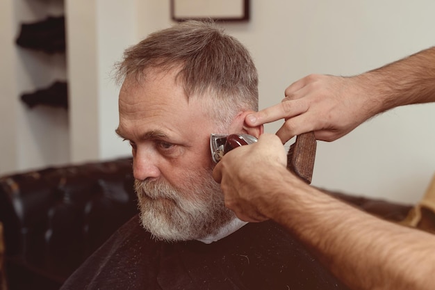 Un vecchio si gode il taglio di capelli da un maestro in un barbiere Un vecchio si fa tagliare i capelli alla moda