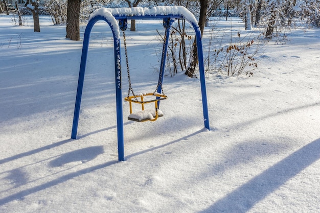 Un vecchio swing per bambini coperto di neve in un parco cittadino. Paesaggio urbano invernale