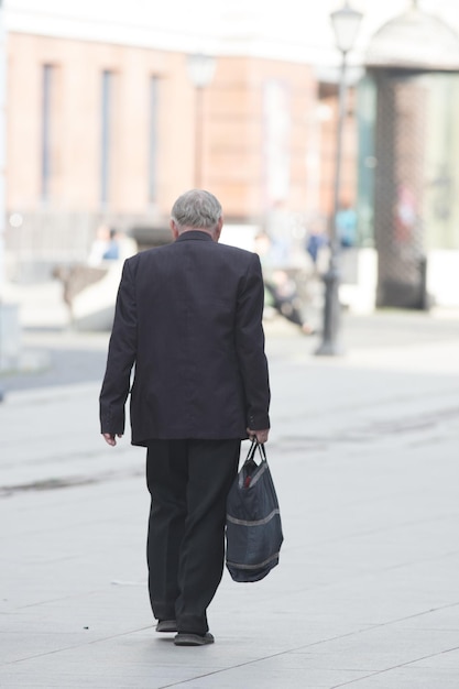 Un vecchio vestito di nero cammina per strada con una tote bag in mano