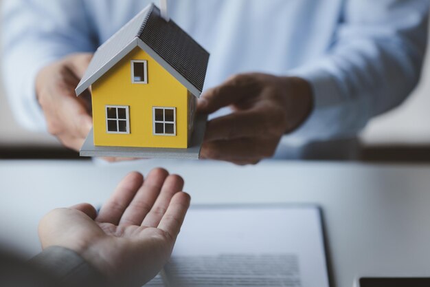 Un venditore di alloggi tiene in mano un modello di casa e lo invia ai clienti come esempio un progetto di casa di esempio in cui un venditore consiglia ai clienti Il concetto di vendita di case nel progetto