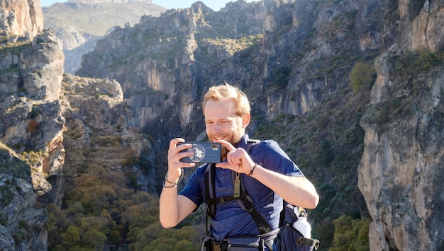 Un viaggiatore maschio caucasico che fotografa la bella vista con le scogliere rocciose dietro di lui