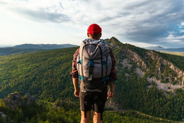 Un viaggiatore sullo sfondo delle montagne. Un turista con uno zaino è in piedi sulla cima della montagna. Un uomo con uno zaino in montagna al tramonto, vista posteriore. Turismo domestico. Copia spazio