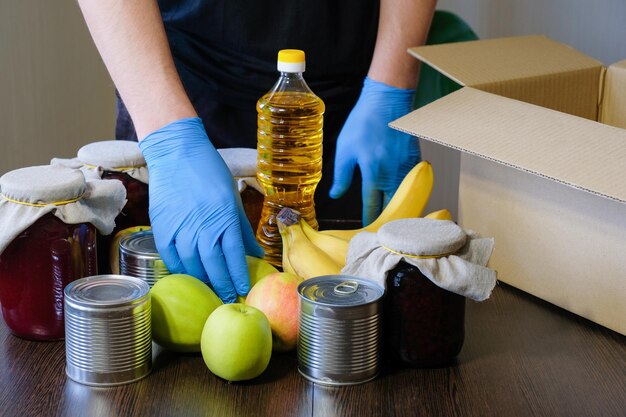 Un volontario che indossa guanti protettivi mette il cibo in una scatola per le donazioni