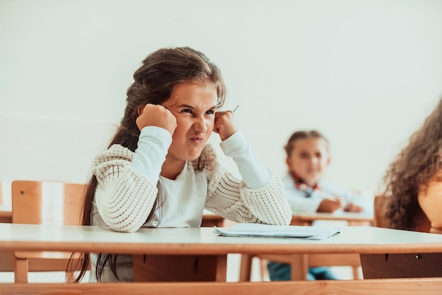 Un volto arrabbiato di una bambina seduta su un banco di scuolaMessa a fuoco selettiva Foto di alta qualità