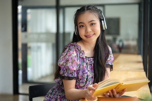 Una affascinante donna asiatica che ascolta musica e legge un libro in un caffè