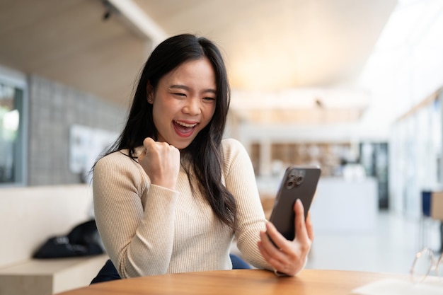 Una allegra donna asiatica guarda lo schermo del suo smartphone con un viso pieno di gioia e di gioia